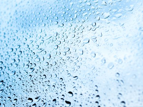 Rain drops on glass. Silhouettes of water drops on blue transparent surface.