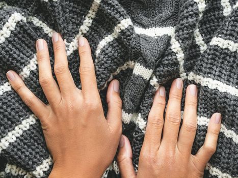 Woman's hands on gray knitted sweater with white stripes. Folded warm clothing. Crumpled textile background.