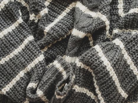 Gray knitted sweater with white stripes. Folded warm clothing. Crumpled textile background.