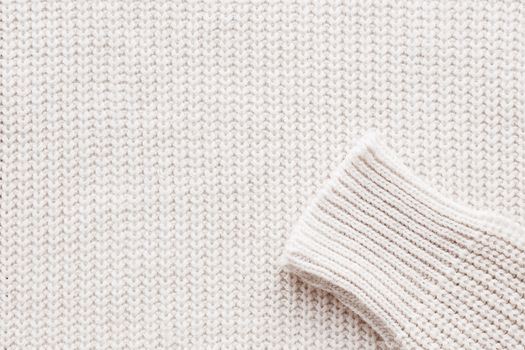 Abstract knitted background. White woolen sweater with sleeves. Close up picture of knitted pattern.