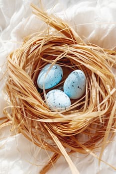 White textile background with bird nest. Decorative straw with blue eggs for Easter celebration.