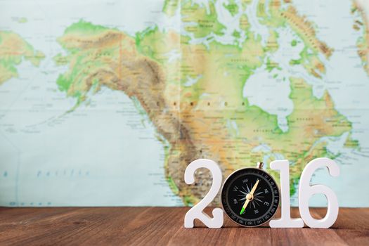 Travel in 2016 year. Numbers 2016 with magnetic compass. Blurred world map as background. Place for text.