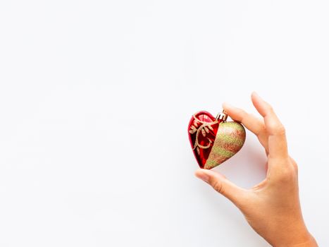 Woman is holding New Year decoration - red heart on white background. Top view on decoration for Christmas tree.