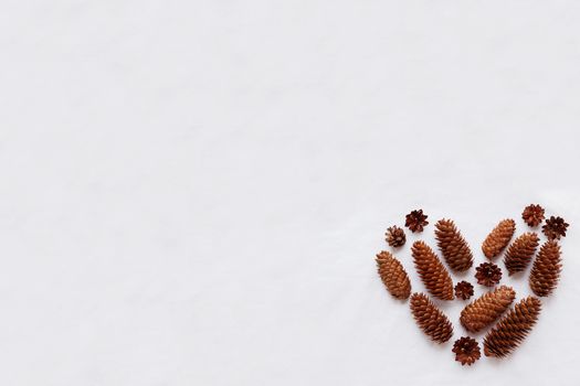 Heart of pine cones and fir cones on white fabric background. Place for your text.