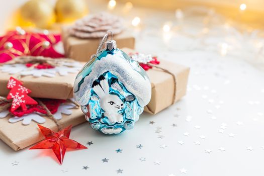 Christmas and New Year background with toy rabbit house, presents and decorations for Christmas tree. Holiday background with stars confetti and light bulbs. Place for text.