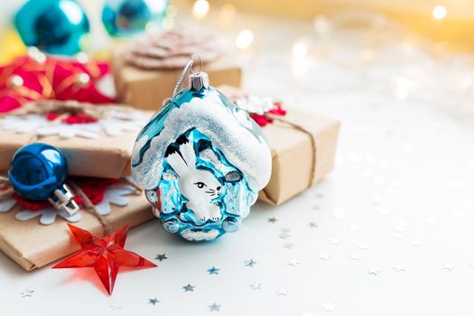 Christmas and New Year background with toy rabbit house, presents and decorations for Christmas tree. Holiday background with stars confetti and light bulbs. Place for text.