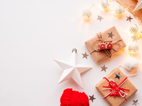 Christmas and New Year wrapped DIY presents in craft paper. Gift tied with rustic thread with toy train as decoration. Metal light bulbs with delicate pattern. Christmas tree decorations.