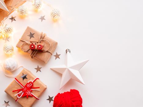 Christmas and New Year wrapped DIY presents in craft paper. Gift tied with rustic thread with toy train as decoration. Metal light bulbs with delicate pattern. Christmas tree decorations.