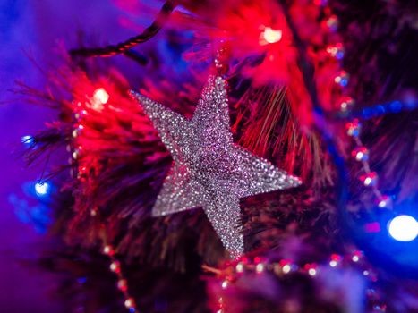 Silver sparkling star on Christmas tree. Colorful light bulbs and decorations on traditional fir tree for New Year celebration.