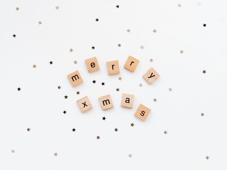 Christmas and New Year background with wooden words MERRY XMAS and star confetti. White copy space.