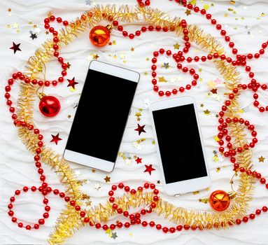 Two smartphones on winter holiday background. Christmas and New Year background with communication devices. Cellulars with christmas decorations - red and yellow tinsel, star sparkles, beads.