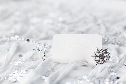 White holiday background with sparkling silver snowflakes, christmas decorations and empty piece of paper for your text.