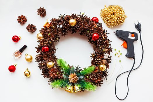 Handmade Christmas wreath and things you need to make it - pine cones, glitter, decorative balls and beads, glue gun.