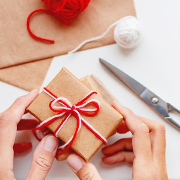 DIY presents wrapped in craft paper. Gifts packed and tied with white and red threads. Boxes in hands on white background.