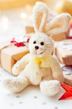 Christmas and New Year background with toy plush rabbit, presents and decorations for Christmas tree. Holiday background with stars confetti and light bulbs.