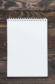 Wooden background with notepad. Clear white page may be used as mock up. Office supply for making notes or to do lists.