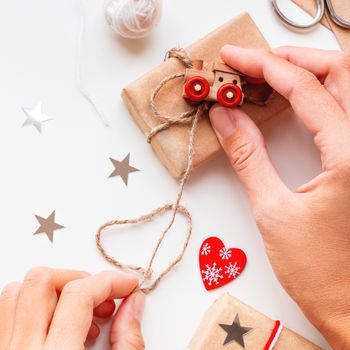 Woman wrapping DIY presents in craft paper. Gifts tied with white and red threads with toy train as decoration.