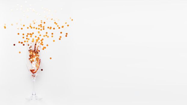 Transparent wine glass with golden spangles. Festive copy space with crockery on white background.