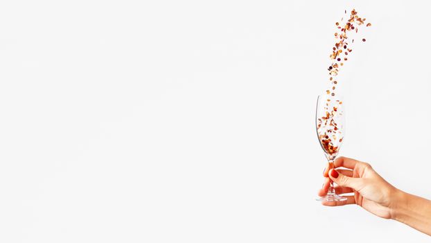 Woman holding transparent wine glass with golden spangles. Festive copy space with crockery on white background.