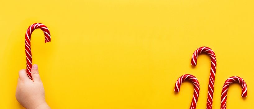 Three Christmas candy cones on yellow background. Colorful holiday sweets with bright copy space. Traditional dessert wtih red and white stripes.