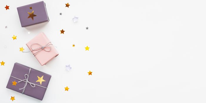 Banner with holiday presents. Gifts wrapped in pale pink and violet paper with silver ribbons and bow. Stars confetti and white copy space.