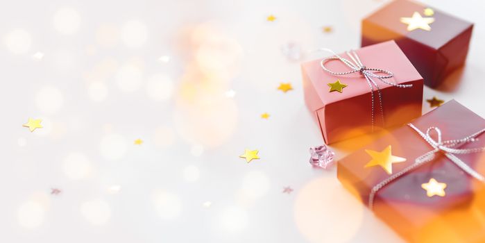 Holiday presents. Gifts wrapped in pale pink and violet paper with silver ribbons and bow. Stars confetti, light bulbs bokeh and white copy space.