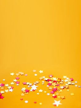 Yellow holiday background with colorful star confetti. Good background for Christmas and New Year cards.