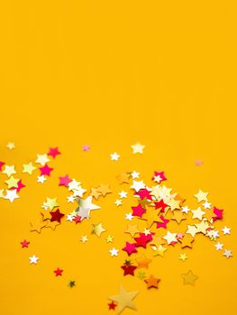 Yellow holiday background with colorful star confetti. Good background for Christmas and New Year cards.