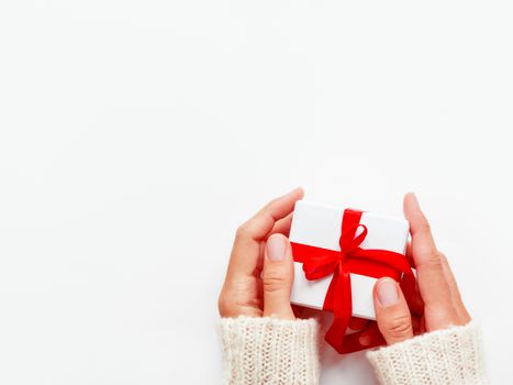 Woman holds a present in white wrapping paper on white backdrop. Holiday gift with red ribbon and bow. Copy space.