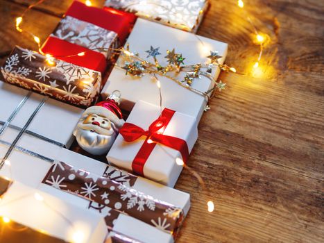 Christmas presents on shabby wooden background. New Year gifts in white and golden paper with bright ribbons and light bulbs.