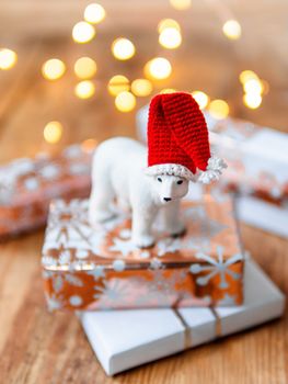 Christmas presents on shabby wooden background. Cute polar bear in Santa's hat standing on New Year gifts in white and golden paper.