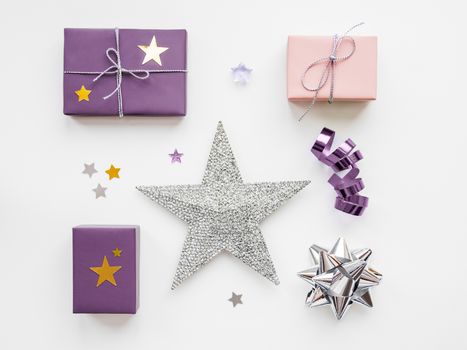 Holiday presents. Gifts wrapped in pale pink and violet paper with silver ribbons and bow. Stars confetti and white copy space. Top view, flat lay.
