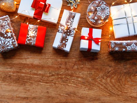 Christmas presents on shabby wooden background. Gifts in white and golden paper with bright ribbons and light bulbs. Top view, flat lay, copy space.