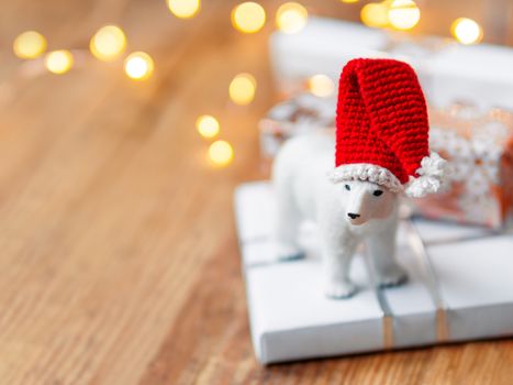 Christmas presents on shabby wooden background. Cute polar bear in Santa's hat standing on New Year gifts in white and golden paper.