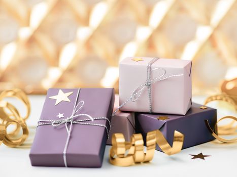 Holiday presents. Gifts wrapped in pale pink and violet paper with silver ribbons. Sparkling golden bows.