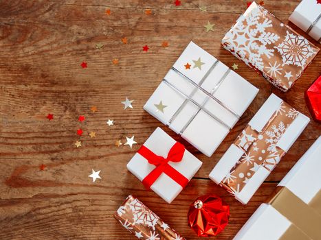 Christmas presentson shabby wooden background. Gifts in white and golden paper with bright golden riboons on with sparkling star confetti. Top view, flat lay.