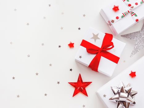 Christmas and New Year background with presents in white wrapping paper. Holiday gifts with red and silver ribbon and bows. Copy space with silver star confetti.