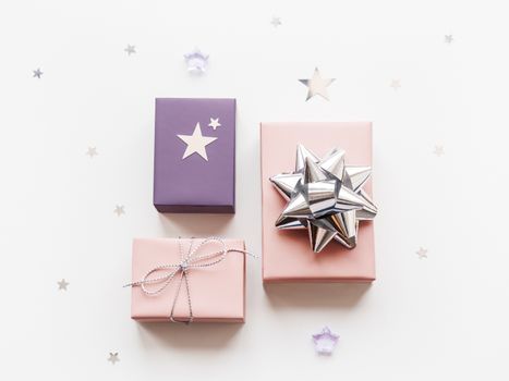 Holiday presents. Gifts wrapped in pale pink and violet paper with silver ribbons and bow. Stars confetti. Top view, flat lay.