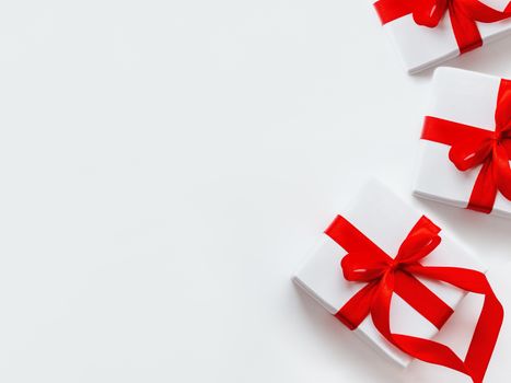 Presents in white wrapping paper on white backdrop. Holiday gifts with red ribbon and bow. Copy space.