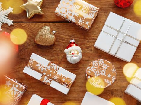 Christmas presents on shabby wooden background. Gifts in white and golden paper with bright ribbons and light bulbs.