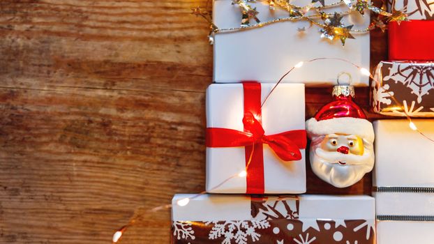 Christmas presents on shabby wooden background. New Year gifts in white and golden paper with bright ribbons and light bulbs.