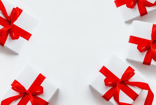 Presents in white wrapping paper on white backdrop. Holiday gifts with red ribbon and bow. Copy space.
