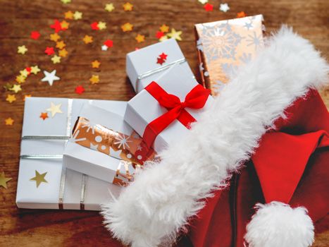 Christmas presents in Santa Claus red hat. Gifts in white and golden paper with bright golden riboons on wooden background with sparkling star confetti.