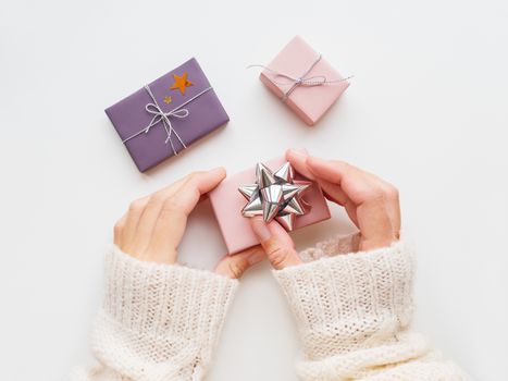 Woman is decorating Christmas present with sparkling silver bow. New Year gifts in pink and violet wrapping paper with shiny star confetti and ribbons. Top view, flat lay.
