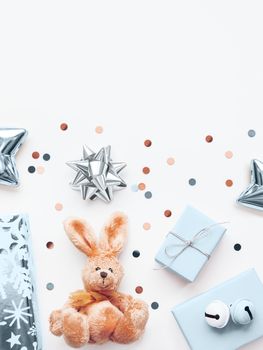Holiday presents in shadows of blue and silver - fluffy toy rabbit, gifts with decorative bells, sparkling confetti, stars. Presents for little boy.