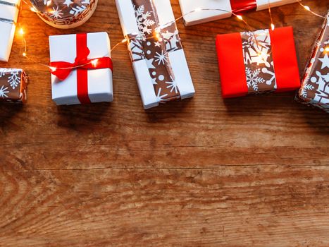 Christmas presents on shabby wooden background. Gifts in white and golden paper with bright ribbons and light bulbs. Top view, flat lay, copy space.