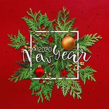 Christmas background with thuja branches and words NEW YEAR 2020 in white square frame. Trendy Xmas greeting with stars and ball decorations on red backdrop.