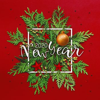 Christmas background with thuja branches and words NEW YEAR 2020 in white square frame. Trendy Xmas greeting with stars and ball decorations on red backdrop.