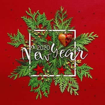 Christmas background with thuja branches and words NEW YEAR 2020 in white square frame. Trendy Xmas greeting with stars and ball decorations on red backdrop.