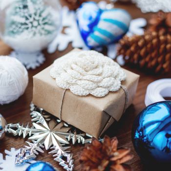 Christmas and New Year background with presents, ribbons, balls and different blue decorations on wooden background. Gift packed in craft paper with hand made crochet flower. DIY way to wrap a present.